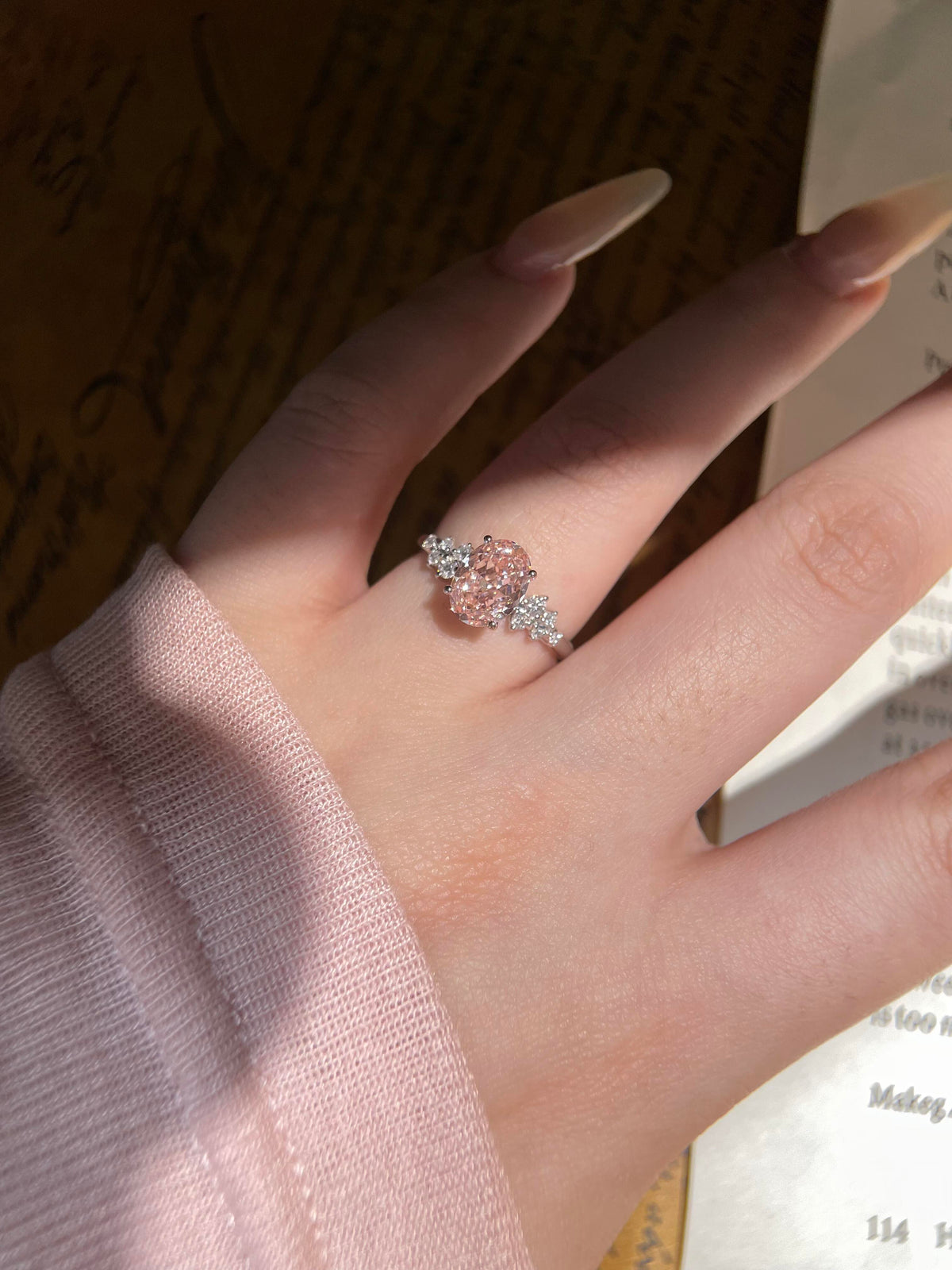 oval pink moissanite engagement ring with sparkling floral side stones.